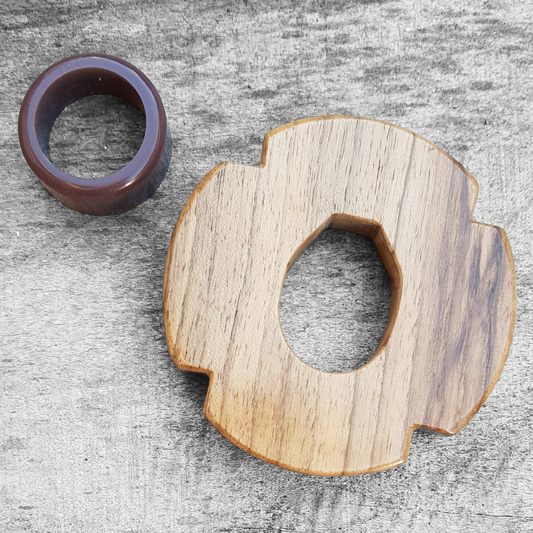 A wooden tsuba for bokken made of walnut wood, displayed on a concrete surface with a rubber stopper in the background.