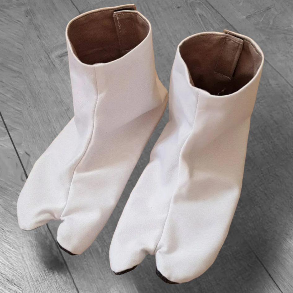 A pair of white split-toe tabi shoes with brown leather soles, designed for aikido and other martial arts, displayed on a wooden floor.