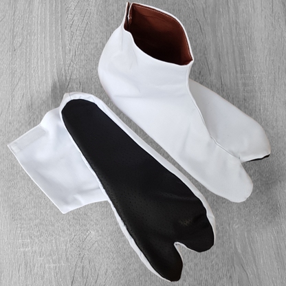 A pair of white split-toe tabi shoes with brown leather soles, designed for aikido and other martial arts, displayed on a wooden floor.