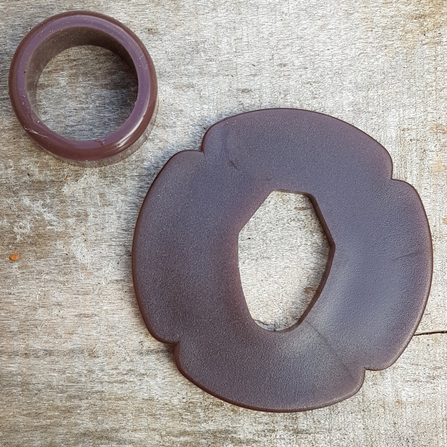 A set of plastic tsuba in black, brown, and beige colors, designed for use with wooden bokken in fencing. The tsuba are in various sizes and shapes, with a four-leaf petal form for protecting the hand.