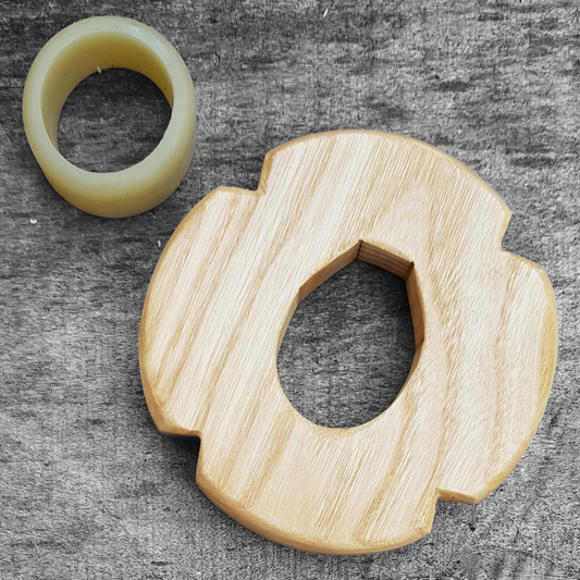 A wooden tsuba, shaped like a four-leaf petal, next to a rubber stopper, both made of European Ash wood.