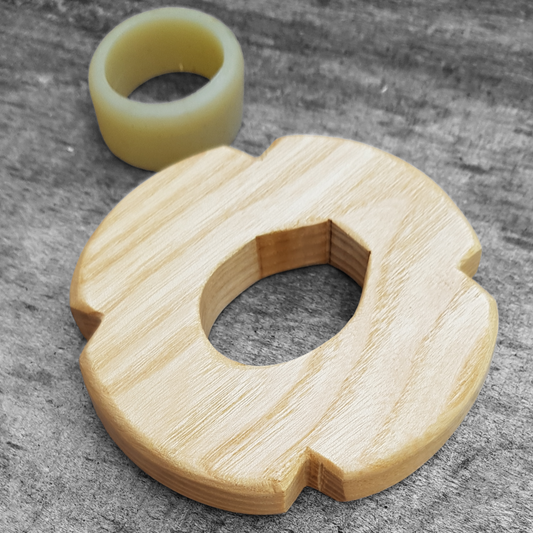 A wooden tsuba, shaped like a four-leaf petal, next to a rubber stopper, both made of European Ash wood.
