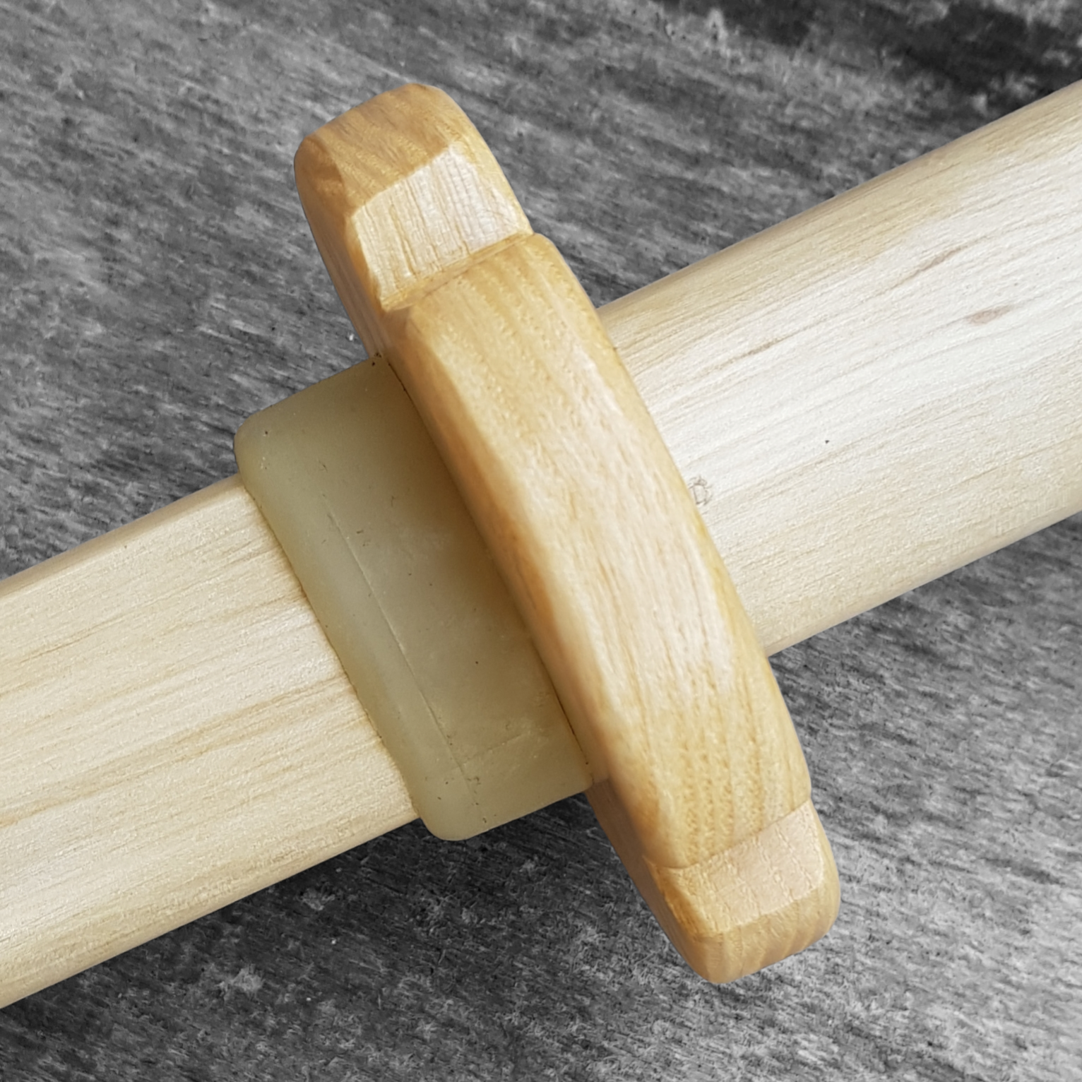 A wooden tsuba, shaped like a four-leaf petal, next to a rubber stopper, both made of European Ash wood.
