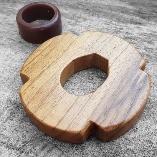 A wooden tsuba for bokken made of walnut wood, displayed on a concrete surface with a rubber stopper in the background.
