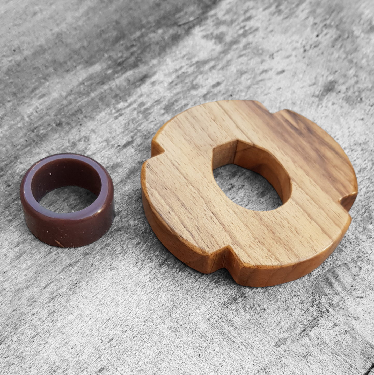 A wooden tsuba for bokken made of walnut wood, displayed on a concrete surface with a rubber stopper in the background.