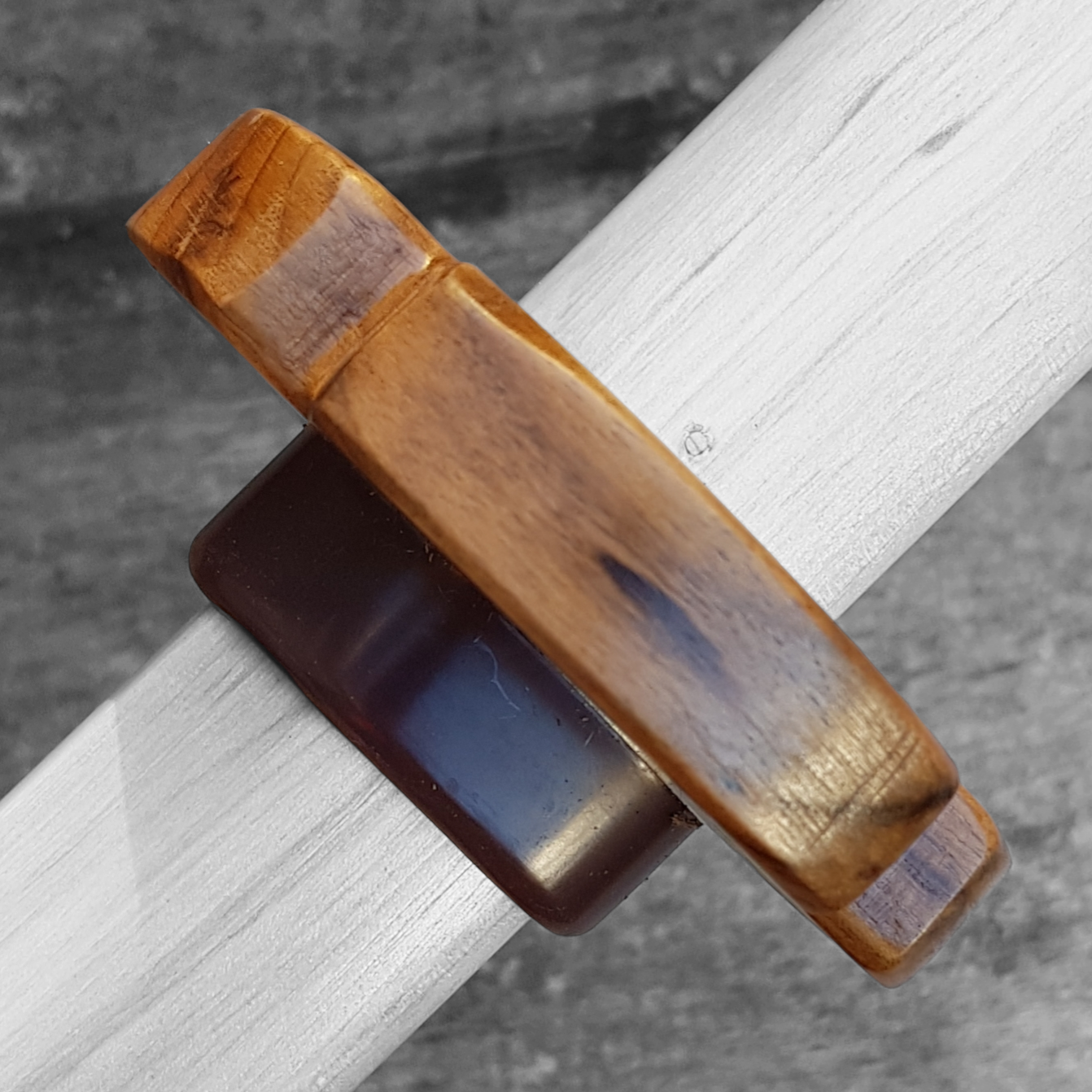A wooden tsuba for bokken made of walnut wood, displayed on a concrete surface with a rubber stopper in the background.