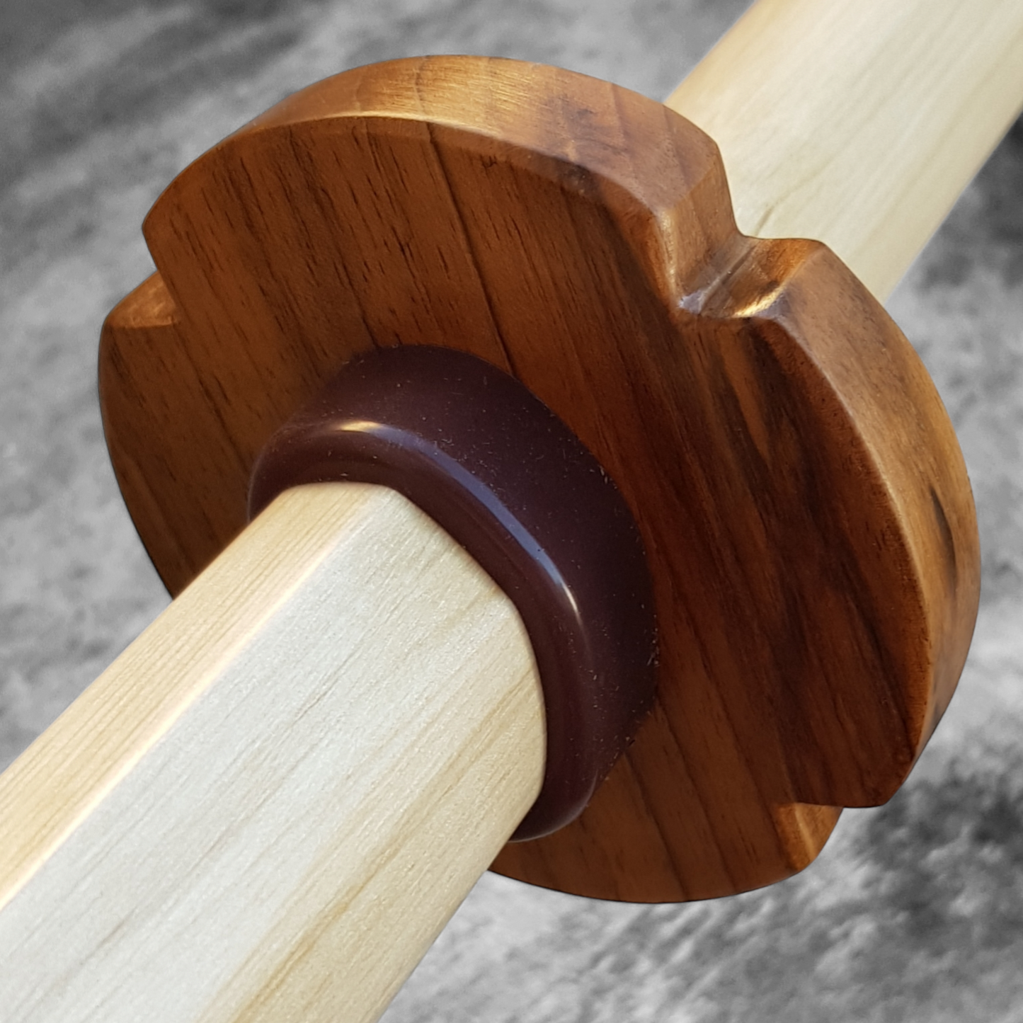 A wooden tsuba for bokken made of walnut wood, displayed on a concrete surface with a rubber stopper in the background.