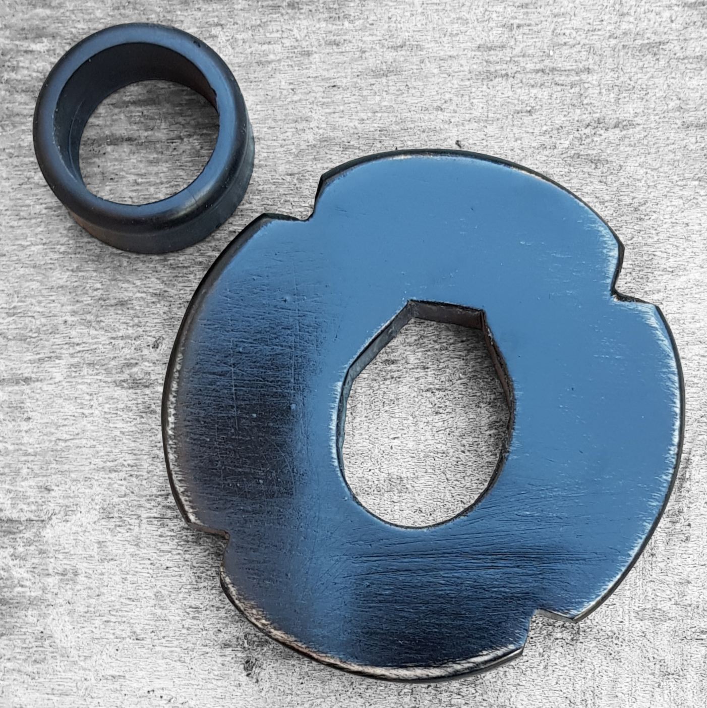 A wooden tsuba, shaped like a four-leaf petal, next to a rubber stopper, placed on a wooden surface.