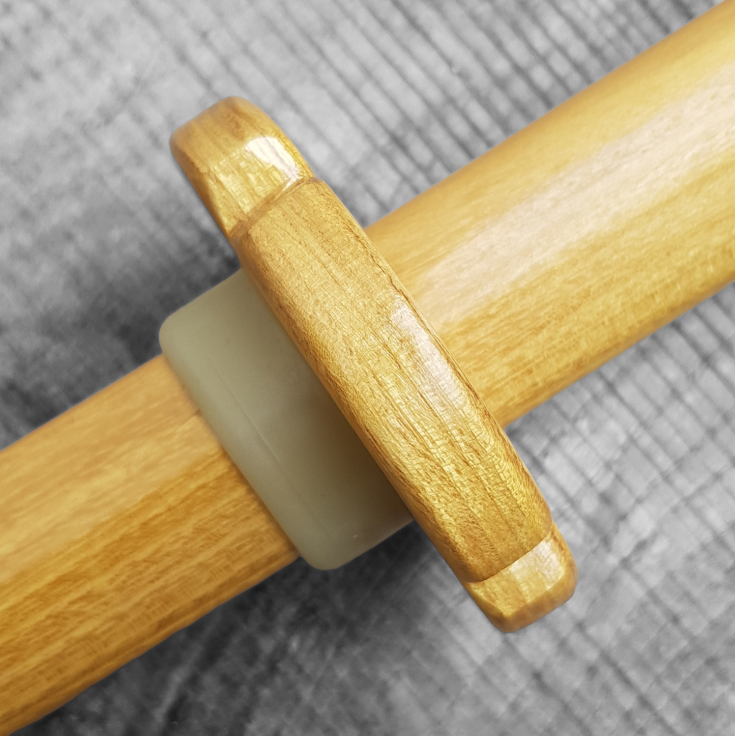 A wooden tsuba, shaped like a four-leaf petal, next to a rubber stopper, placed on a wooden surface.