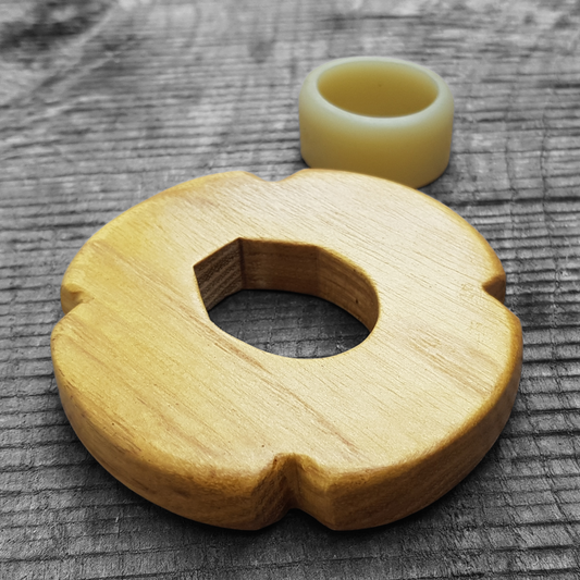 A wooden tsuba, shaped like a four-leaf petal, next to a rubber stopper, placed on a wooden surface.