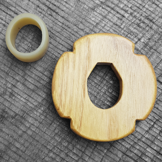 A wooden tsuba, shaped like a four-leaf petal, next to a rubber stopper, placed on a wooden surface.