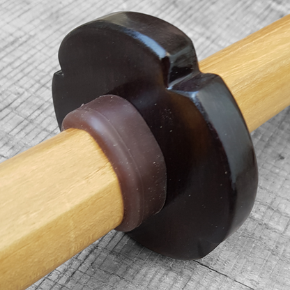 A wooden tsuba, shaped like a four-leaf petal, next to a rubber stopper, both made of European Ash wood.