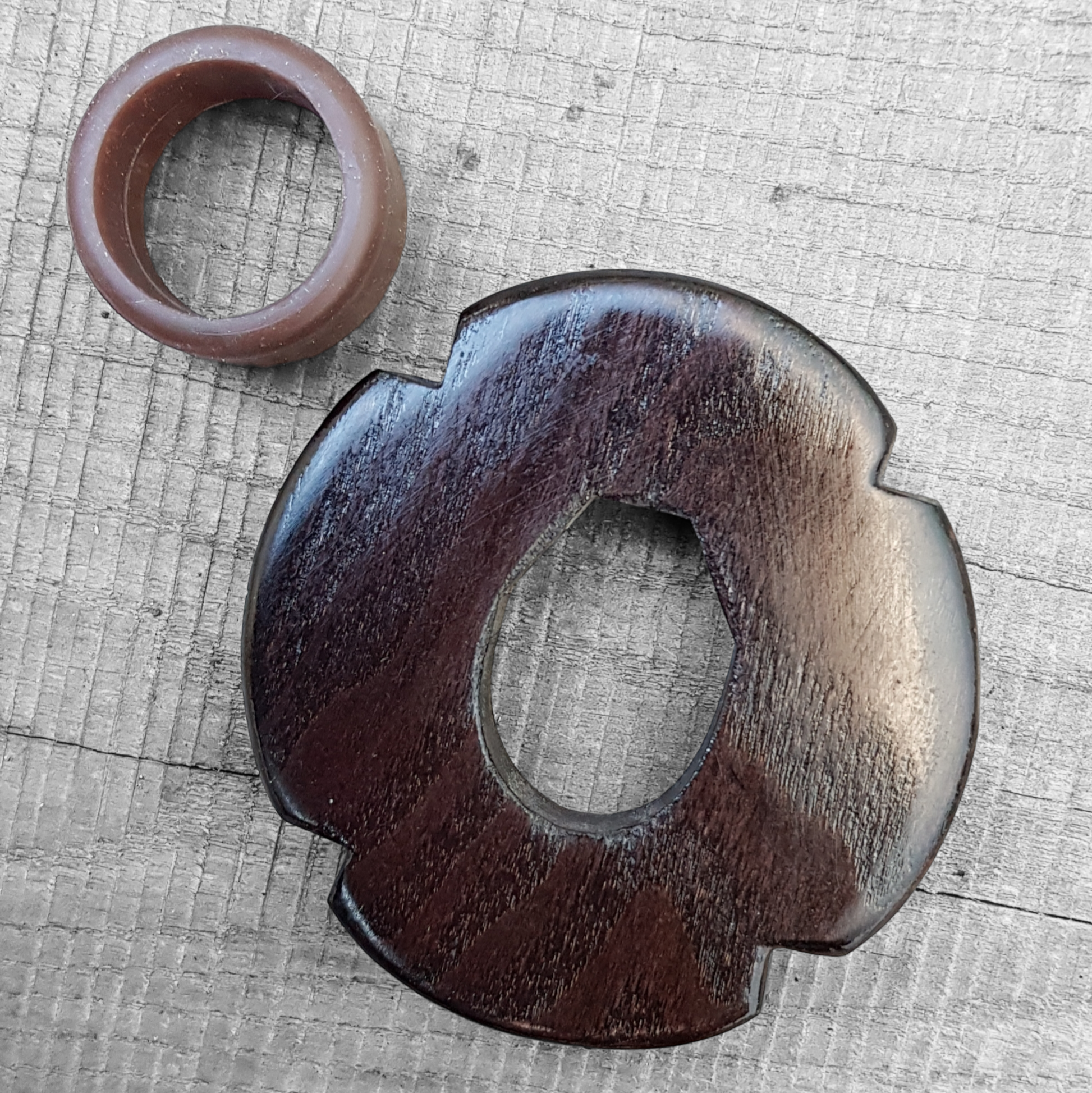 A wooden tsuba, shaped like a four-leaf petal, next to a rubber stopper, both made of European Ash wood.
