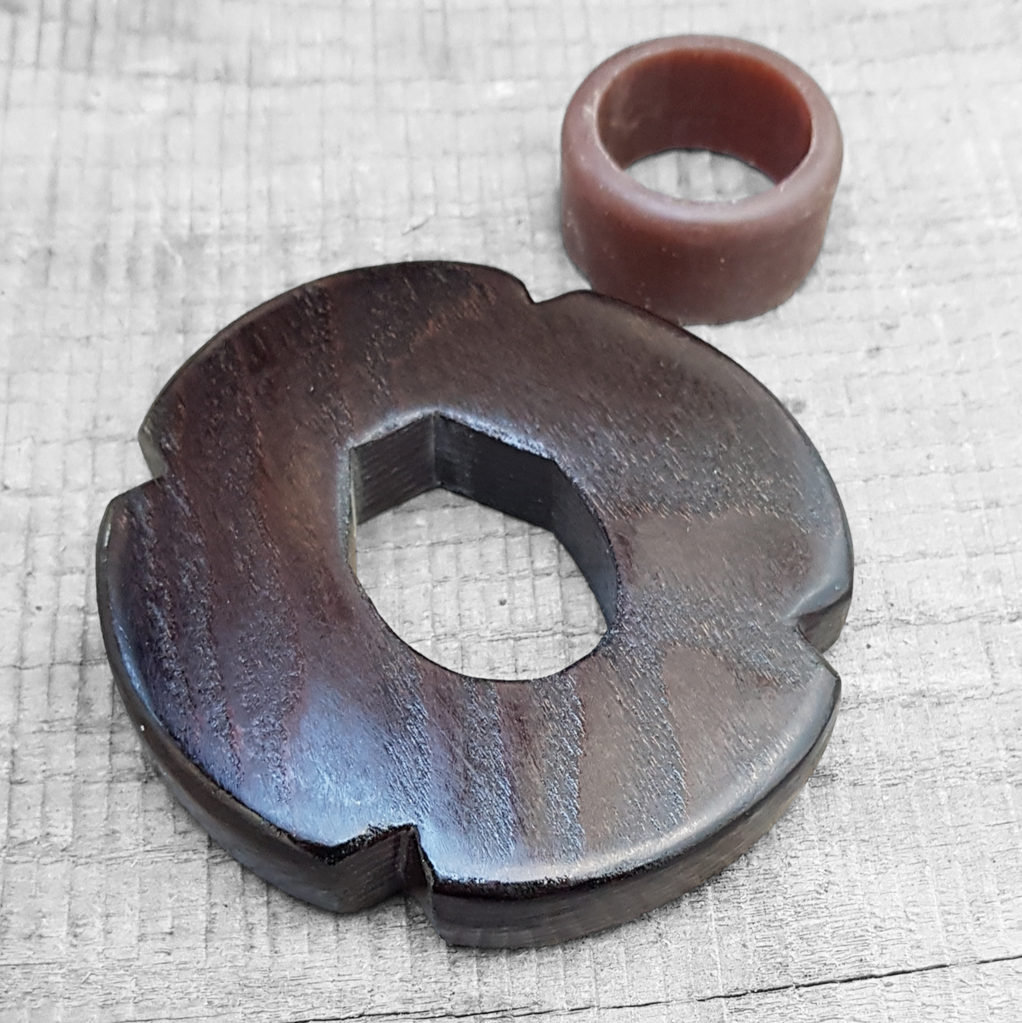 A wooden tsuba, shaped like a four-leaf petal, next to a rubber stopper, both made of European Ash wood.