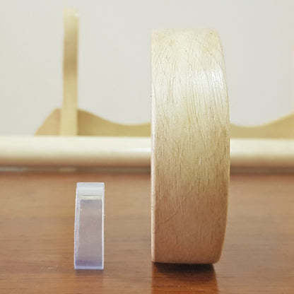 A wooden tsuba, which is a type of protective cover, placed next to a clear plastic clamp on a wooden surface.