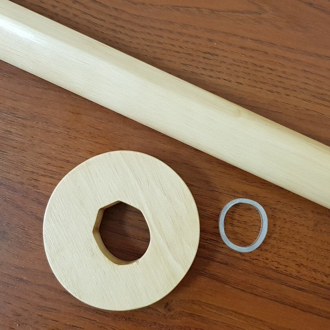 A wooden tsuba, which is a type of protective cover, placed next to a clear plastic clamp on a wooden surface.