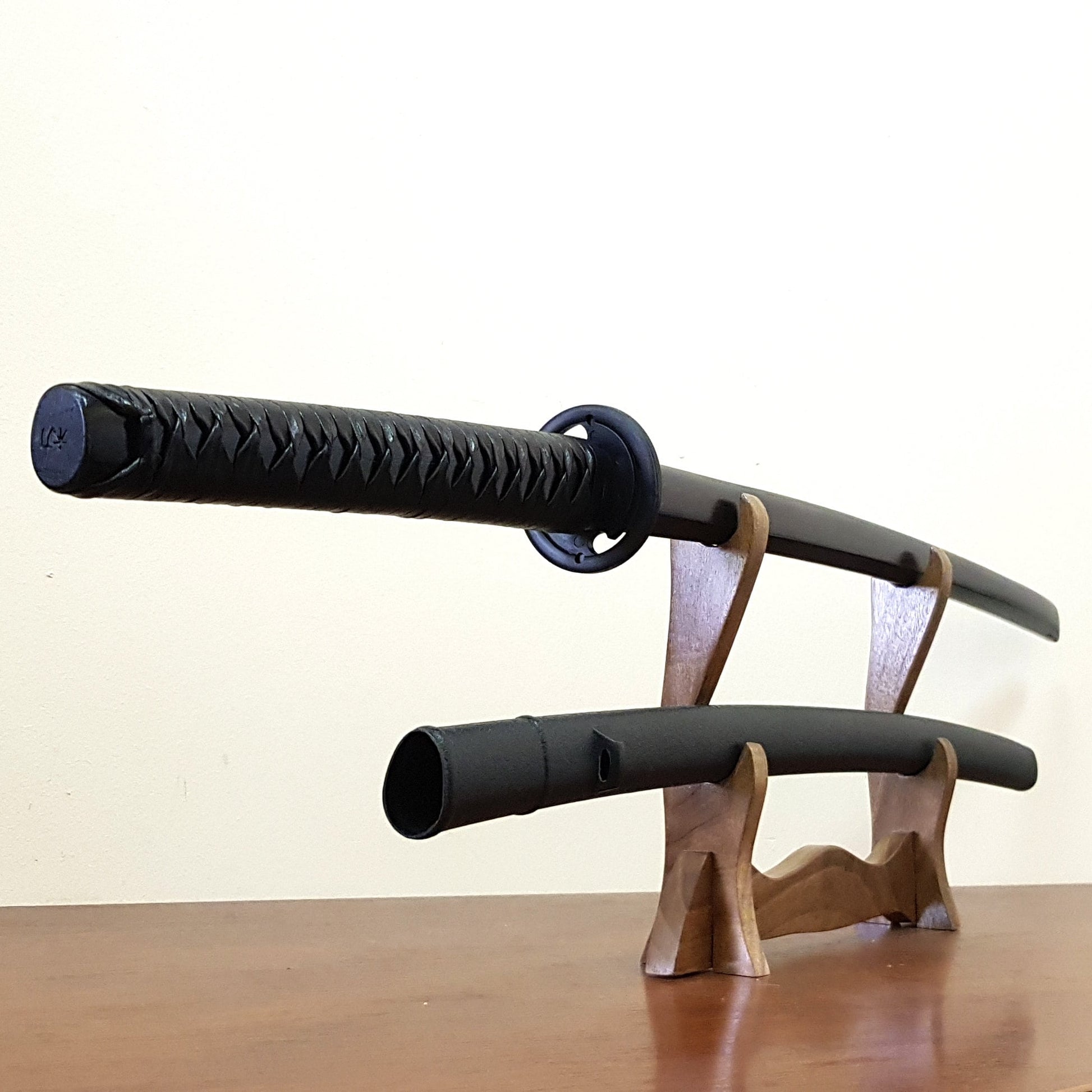 A bokken (wooden sword) with a patterned rubber tsuba and plastic saya displayed on a wooden stand. The bokken has a black tsukamaki (hand grip) and the overall length is 102 cm.